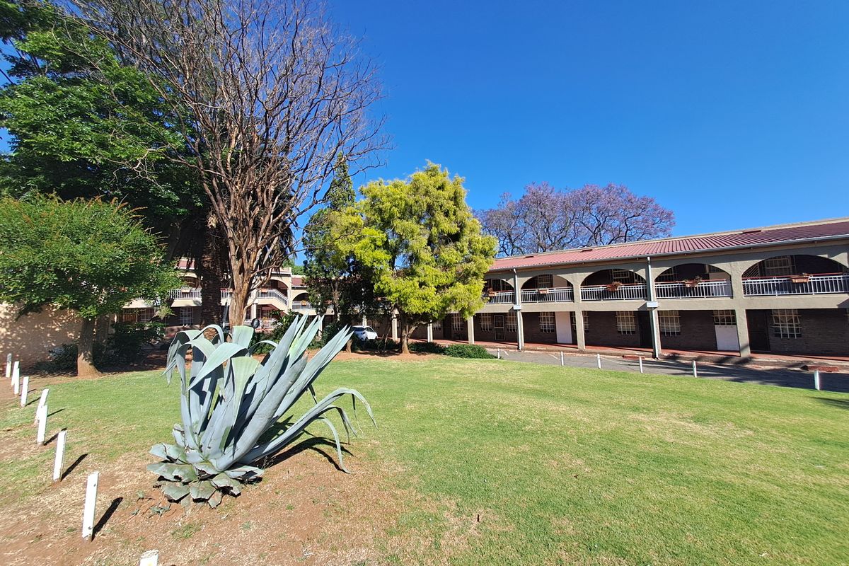 Exterior view of the apartment complex featuring a landscaped garden area, mature trees, and a multi-level building with arched balcony walkways.