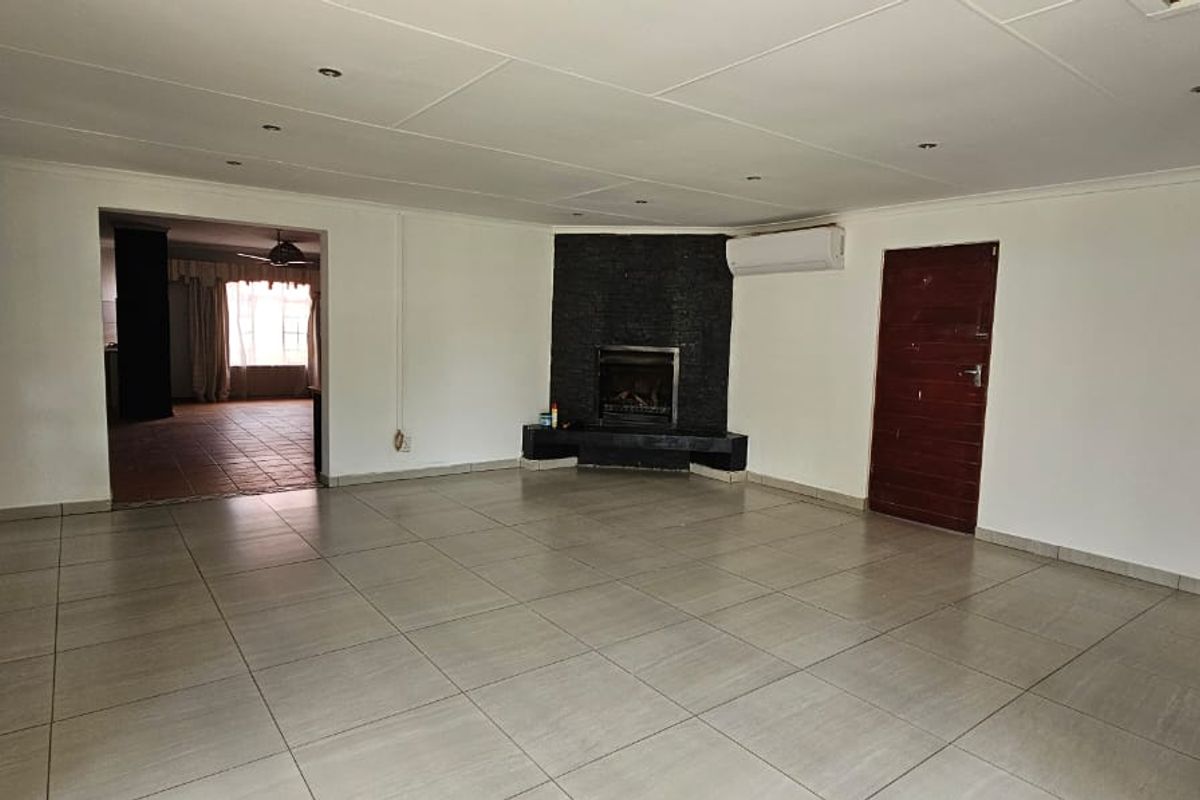 Spacious, empty living room featuring large format floor tiles, a built-in fireplace with stone cladding, and a wall-mounted air conditioning unit.