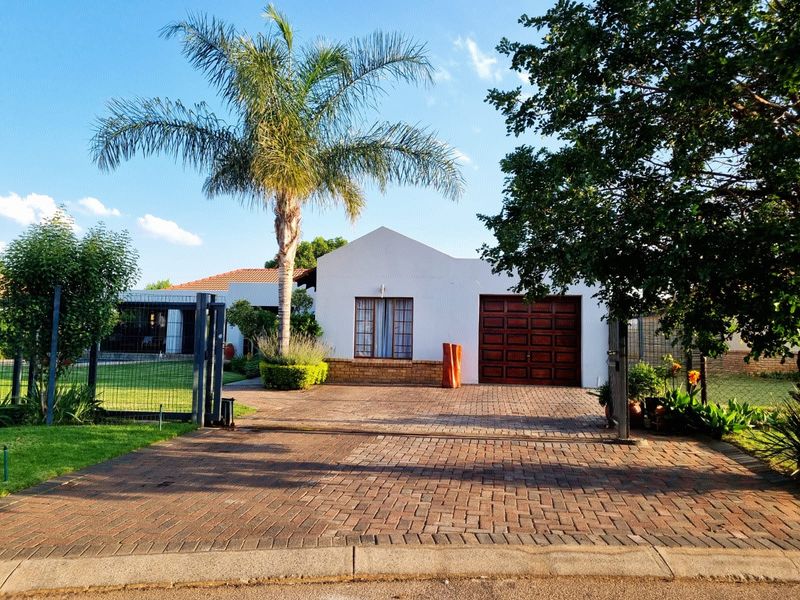 Front view of a residential house featuring a paved driveway, secure metal gate, wooden garage door, and established garden landscaping.