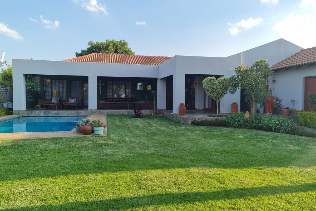 A well-maintained rear exterior view featuring a swimming pool, a spacious covered patio area, and a neatly landscaped garden.
