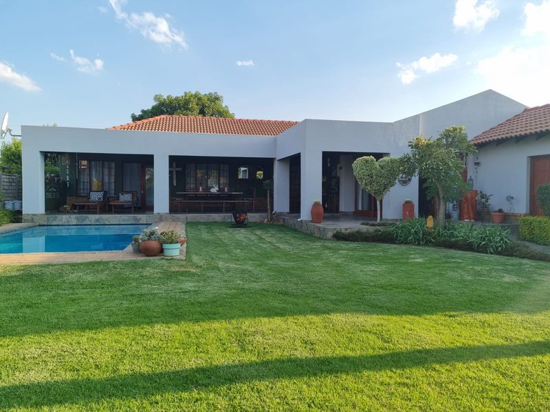 A well-maintained rear exterior view featuring a swimming pool, a spacious covered patio area, and a neatly landscaped garden.