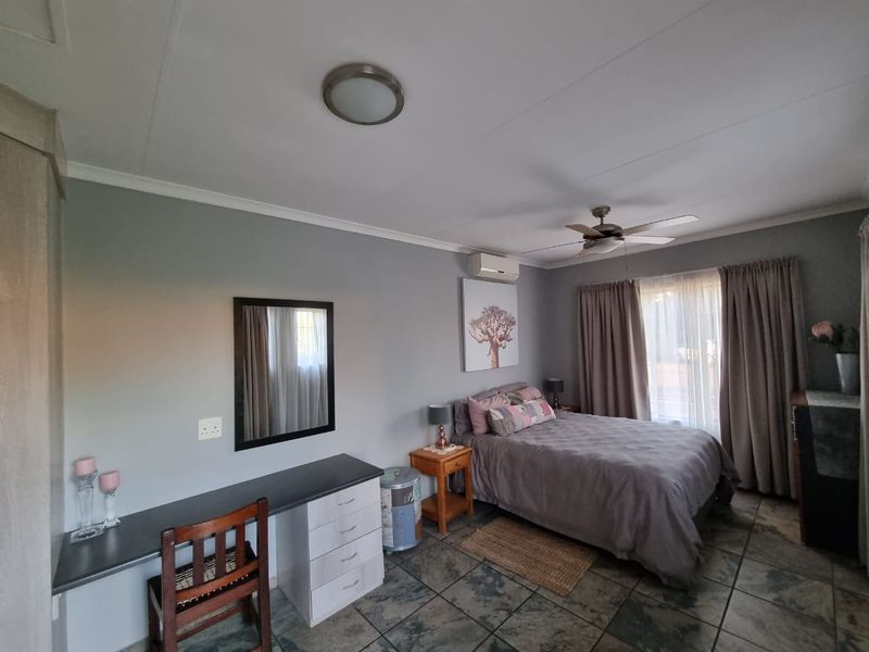 A well-maintained bedroom featuring tiled flooring, a ceiling fan, a split-system air conditioner, and built-in desk cabinetry.