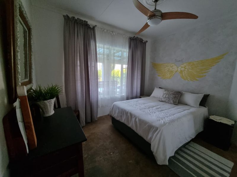 A bedroom featuring a ceiling fan with a decorative rose and large window with curtain tracks, providing natural light.