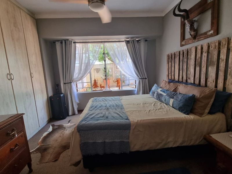 A cozy bedroom featuring built-in cupboards, a ceiling fan, and a large window providing natural light.