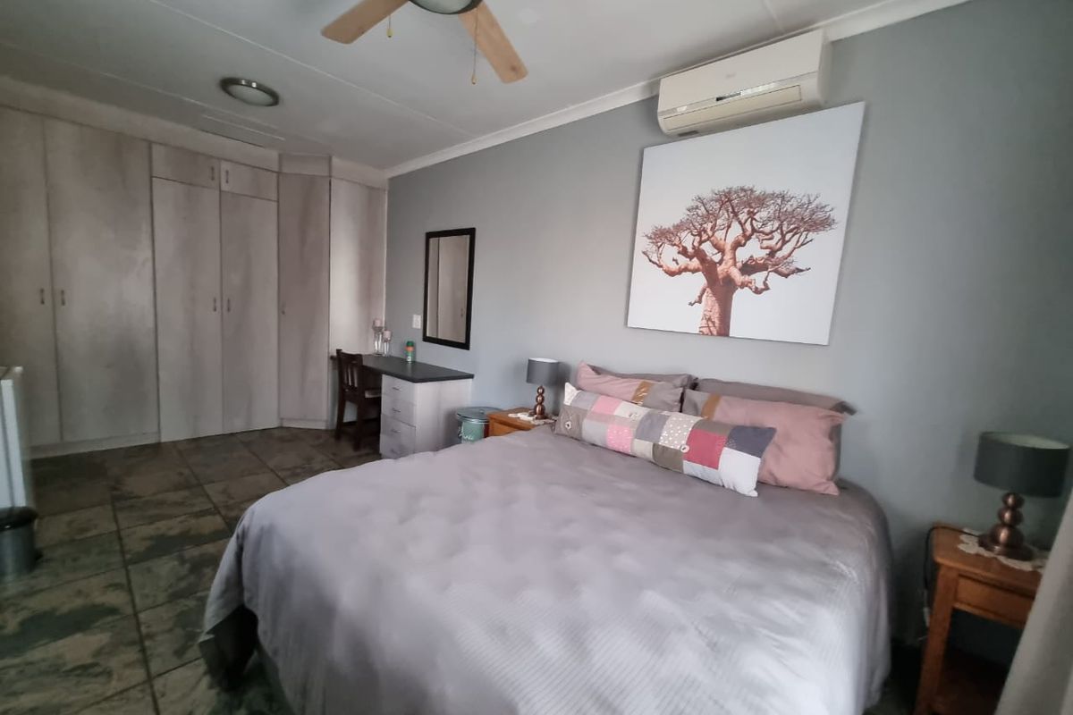 A well-maintained bedroom featuring built-in cupboards, tiled flooring, a ceiling fan, and a wall-mounted split-system air conditioner.