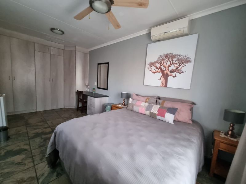 A well-maintained bedroom featuring built-in cupboards, tiled flooring, a ceiling fan, and a wall-mounted split-system air conditioner.