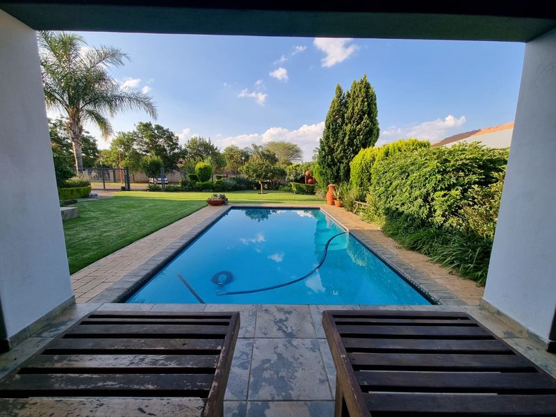 A well-maintained swimming pool set within a landscaped garden, viewed from a covered patio area.
