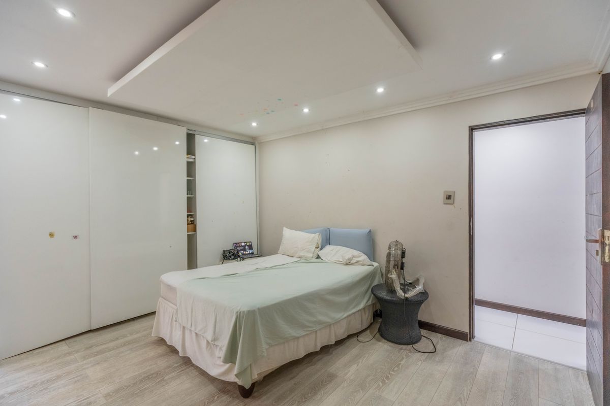 A bedroom featuring laminate flooring, a large built-in sliding wardrobe, and a modern recessed ceiling design with integrated downlights.