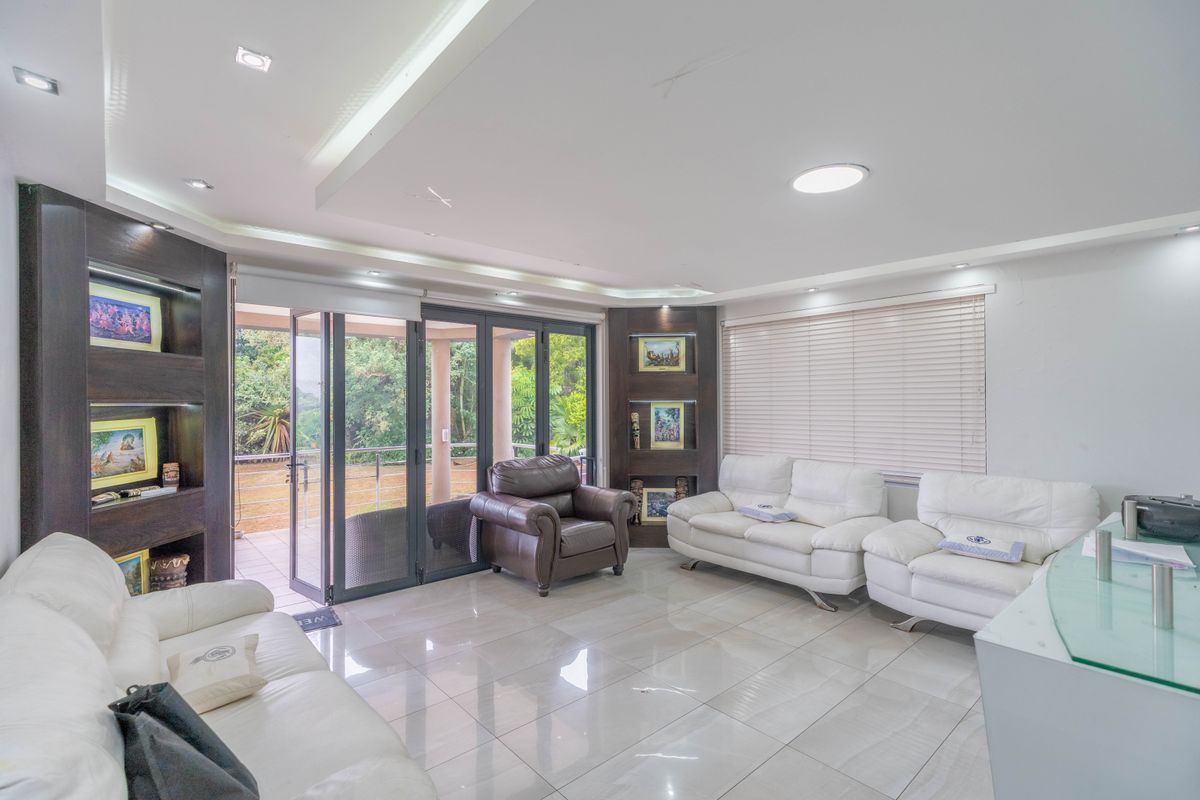 Spacious living room featuring tiled flooring, recessed ceiling lighting, built-in display shelving, and large aluminium stacker doors opening to an outdoor patio area.