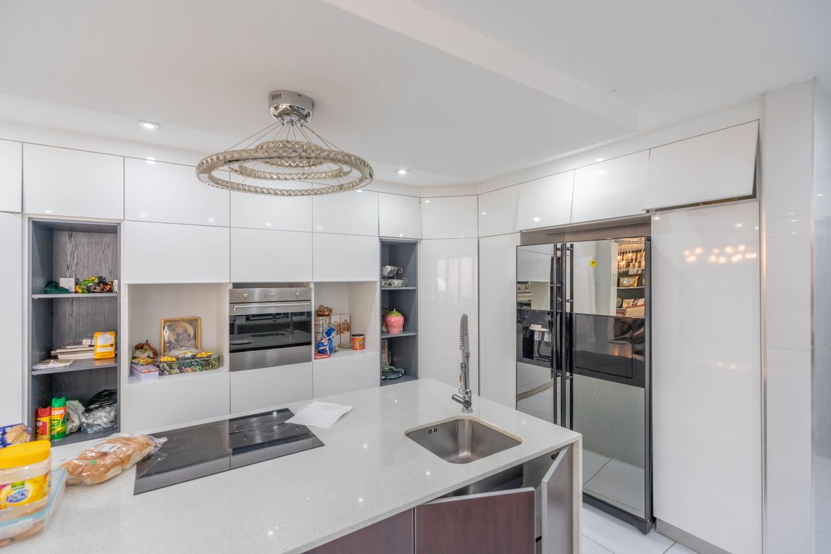 Modern kitchen featuring high-gloss white cabinetry, stone countertops, an integrated refrigerator, and a central island with a built-in induction hob and sink.