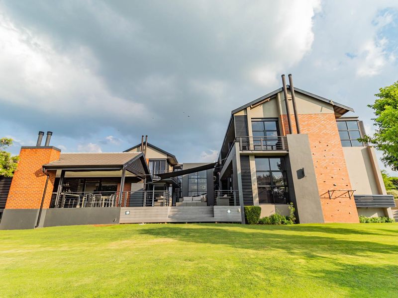 A modern architectural rear elevation featuring brick and render finishes, a spacious timber deck, and a built-in climbing wall overlooking a manicured lawn.