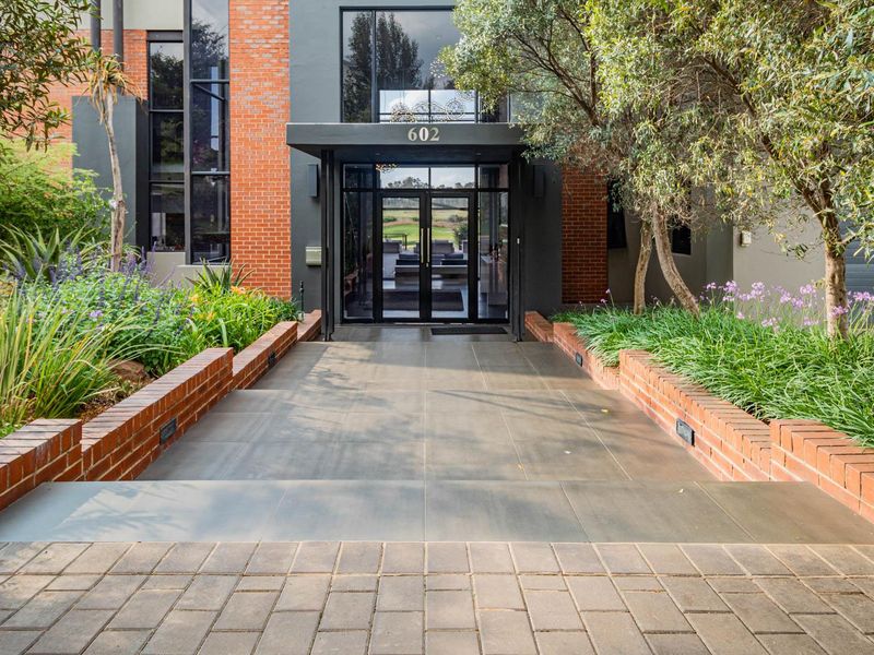 Modern front entrance featuring a striking brick and glass facade, tiled walkway, and landscaped brick planter boxes leading to a contemporary glass door.