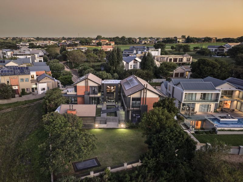 Aerial view of a modern multi-level residential property featuring brick and metal architecture, solar panels, and a spacious landscaped garden with decking.