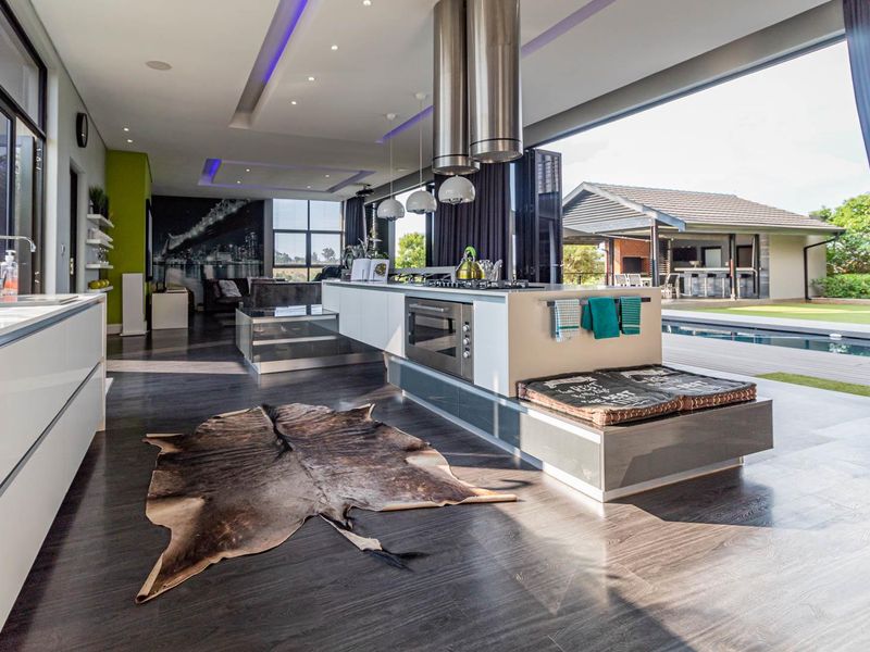 Modern open-plan kitchen featuring a large island with built-in appliances, sleek cabinetry, and seamless indoor-outdoor flow through expansive sliding glass doors.