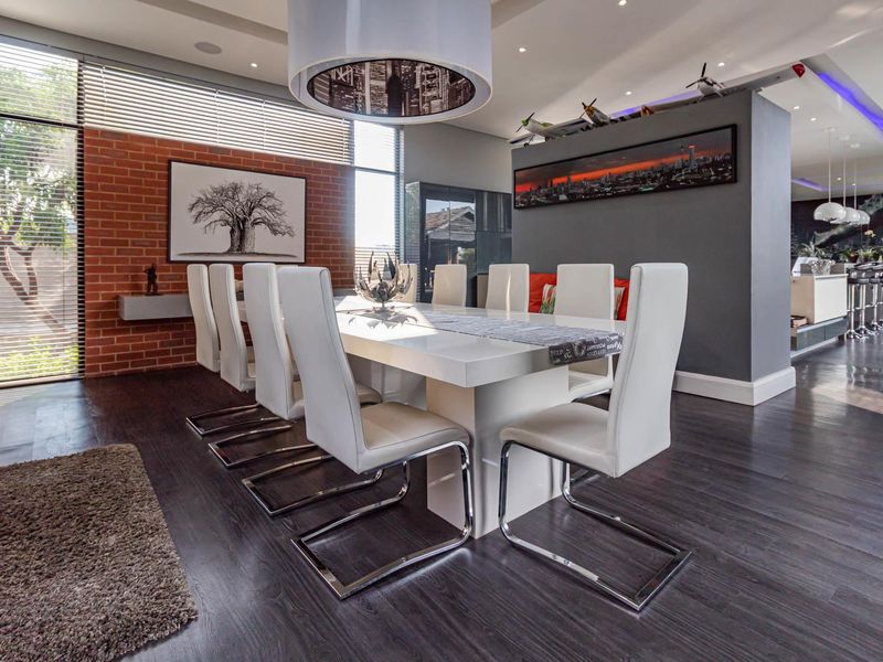 Modern open-plan dining area featuring dark laminate flooring, an exposed brick feature wall, and seamless flow into the adjacent kitchen space.