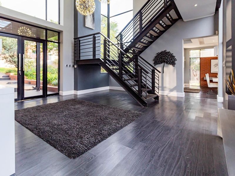 Spacious modern entrance hall featuring a striking metal staircase, high ceilings, floor-to-ceiling windows, and sleek dark laminate flooring.