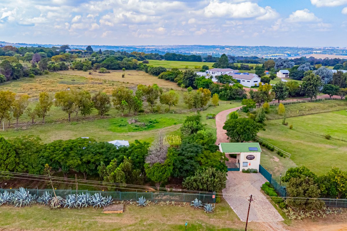 An aerial view of a residential property featuring a gated entrance, paved driveway, and expansive landscaped grounds within a rural setting.