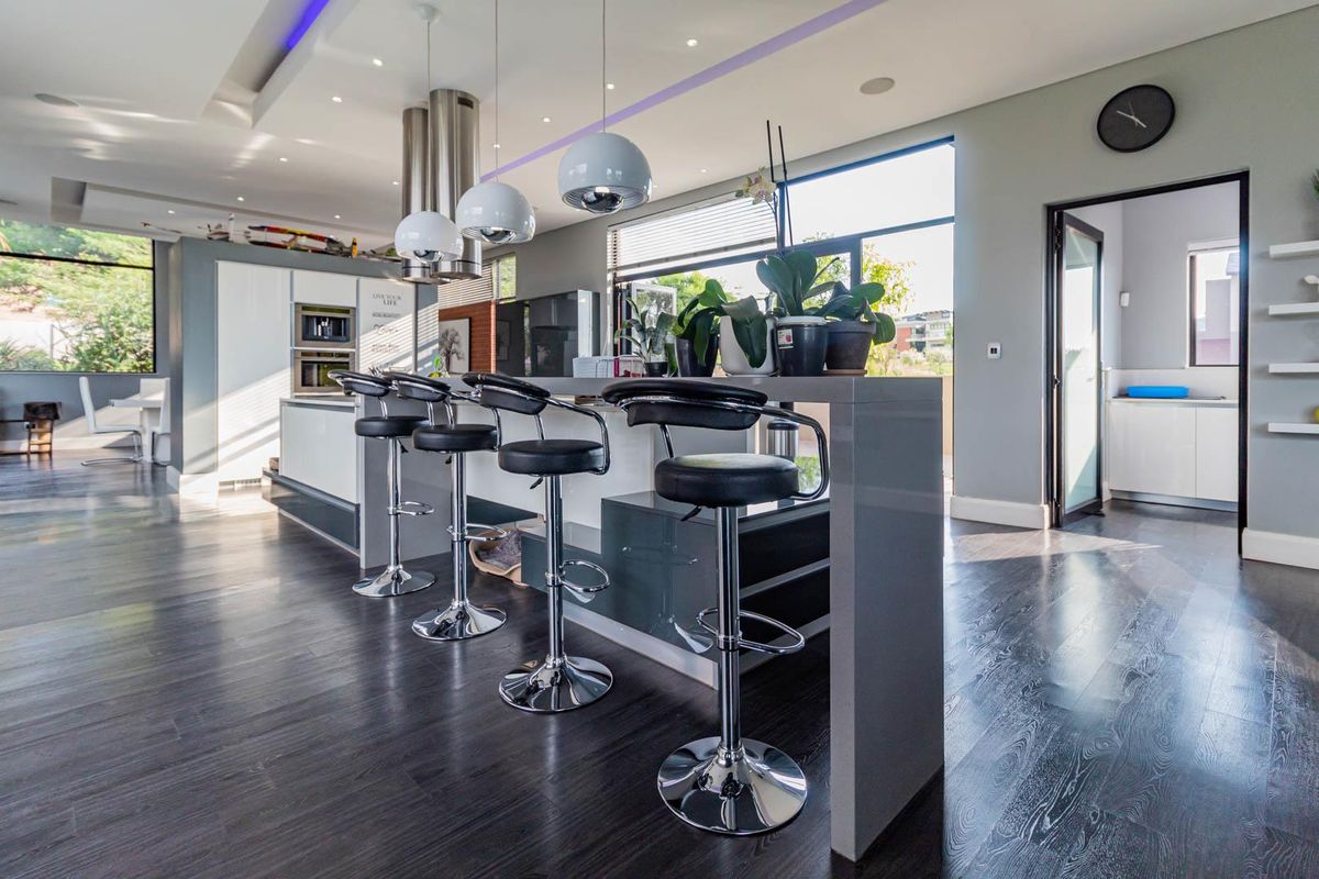 Modern kitchen featuring a large island with breakfast bar seating, integrated appliances, sleek cabinetry, and contemporary recessed and cove lighting.