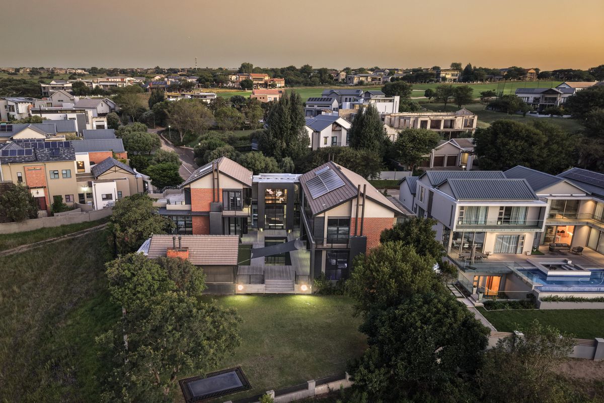 Aerial view of a modern multi-level residential property featuring brick and metal architecture, solar panels, and a spacious landscaped garden with decking.
