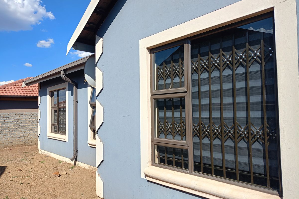 Side exterior view of the house featuring blue painted walls, white corner detailing, and aluminium window frames with fitted security gates.