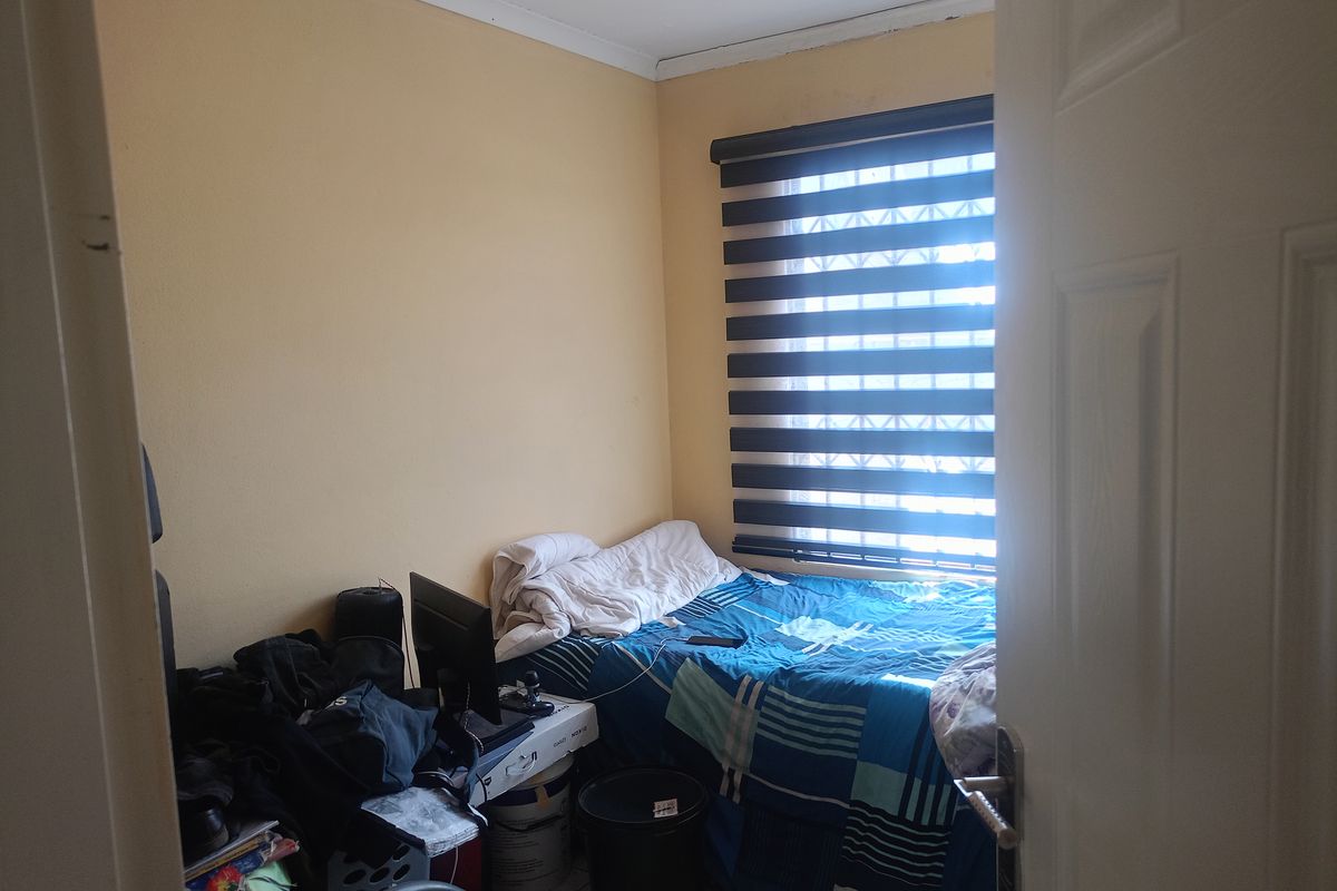 A compact bedroom featuring tiled flooring, a window with fitted zebra blinds, and standard interior door access.