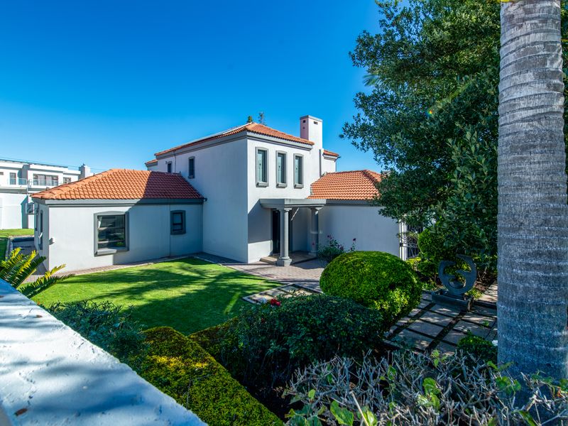 A well-maintained rear exterior view of the house featuring a terracotta tiled roof, paved pathways, and a manicured garden.