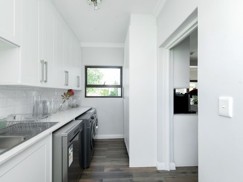 A clean and modern laundry room featuring white cabinetry, subway tile backsplash, stainless steel sink, and durable wood-look laminate flooring.