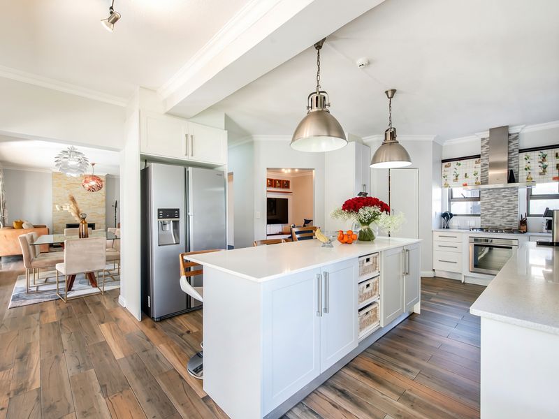 Modern open-plan kitchen featuring a central island with stone countertops, high-end built-in appliances, and elegant pendant lighting, seamlessly flowing into the adjacent living area.