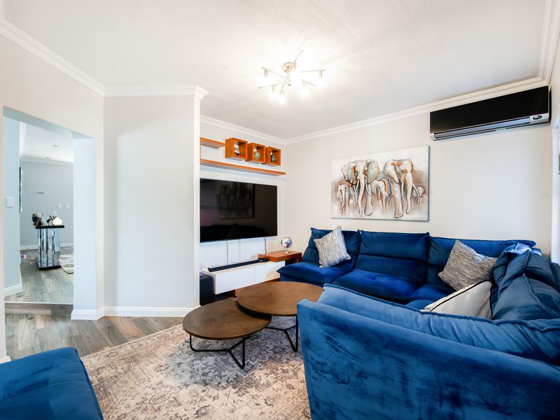 A well-maintained living room featuring laminate flooring, built-in shelving, and a wall-mounted split-system air conditioner.
