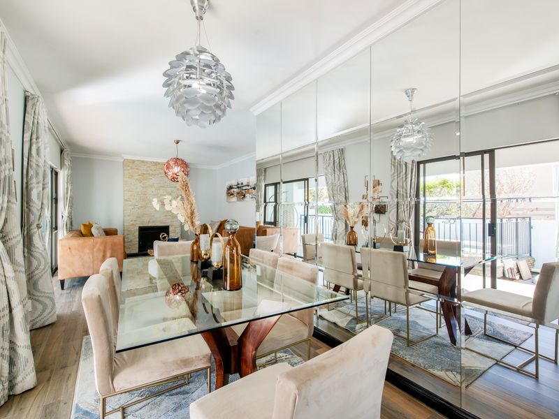 Elegant dining room featuring a stone-clad fireplace, hardwood flooring, and a large mirrored wall that enhances the sense of space and light.