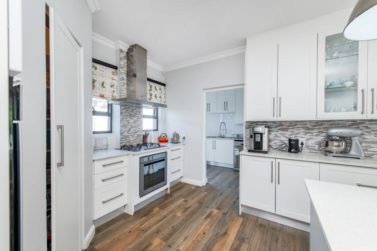 Modern kitchen featuring white cabinetry, stone countertops, mosaic backsplash, gas hob, and integrated oven, with an adjacent scullery area visible.