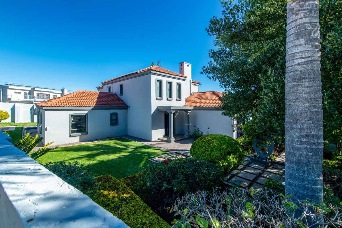 A well-maintained rear exterior view of the house featuring a terracotta tiled roof, paved pathways, and a manicured garden.