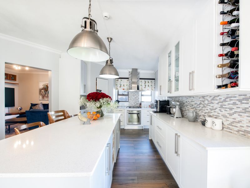 Modern kitchen featuring white cabinetry, stone countertops, a central island, built-in oven, extractor fan, and a stylish mosaic tile backsplash.