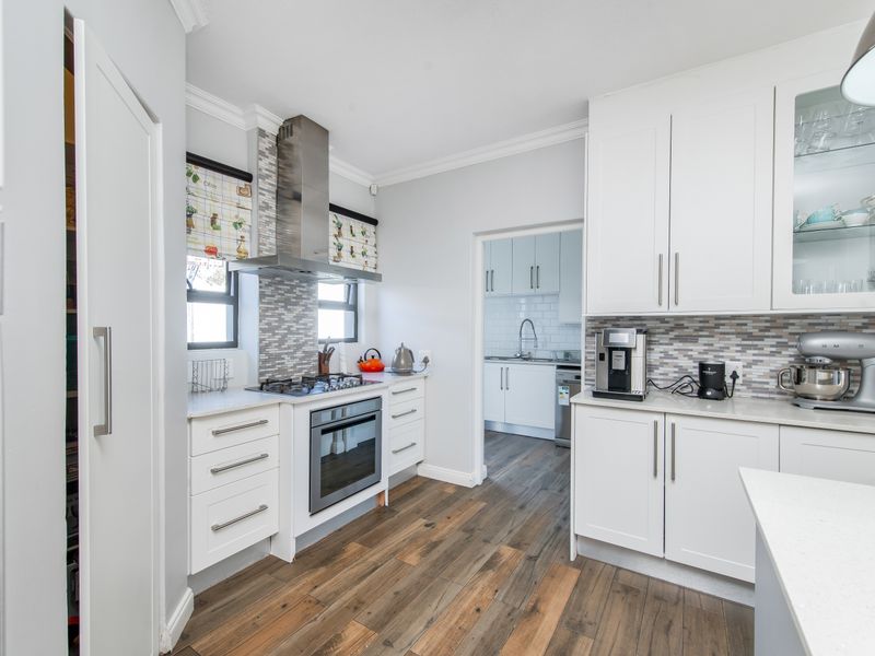Modern kitchen featuring white cabinetry, stone countertops, mosaic backsplash, gas hob, and integrated oven, with an adjacent scullery area visible.
