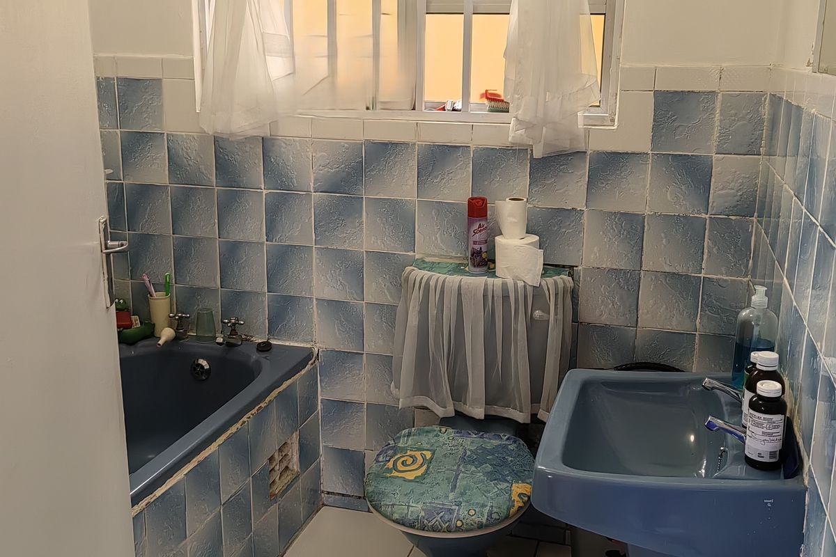 A dated bathroom featuring blue sanitaryware, tiled walls, and a security gate on the window. Ideal for a modern renovation.