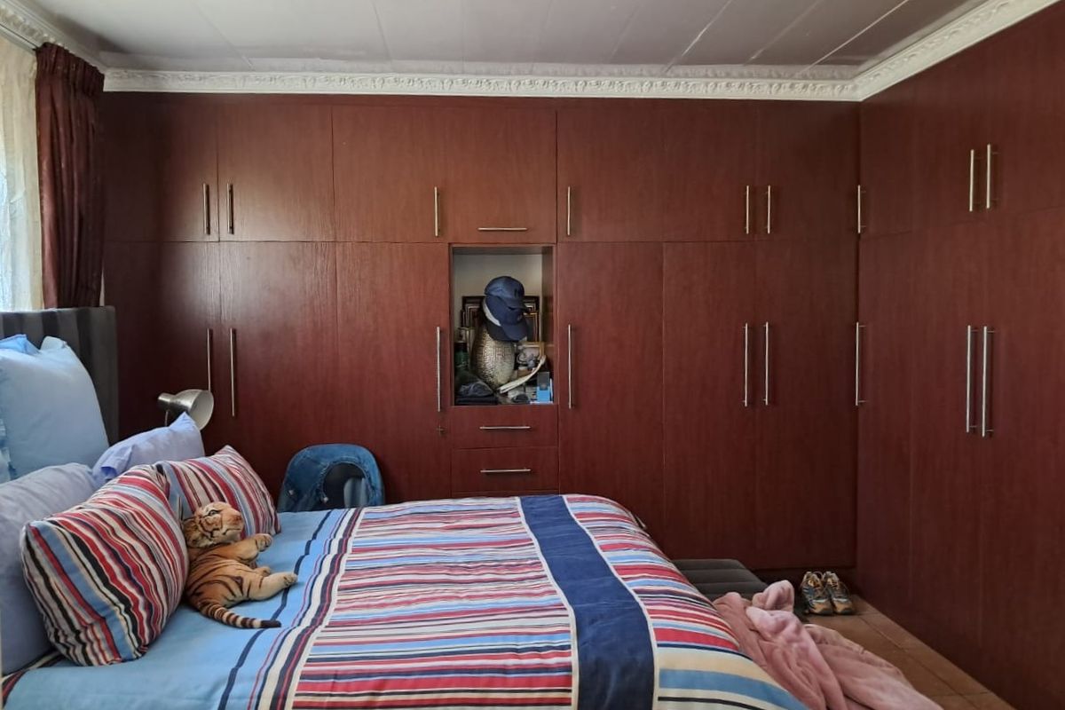 A bedroom featuring extensive floor-to-ceiling built-in wooden cupboards, decorative ceiling cornices, and tiled flooring.