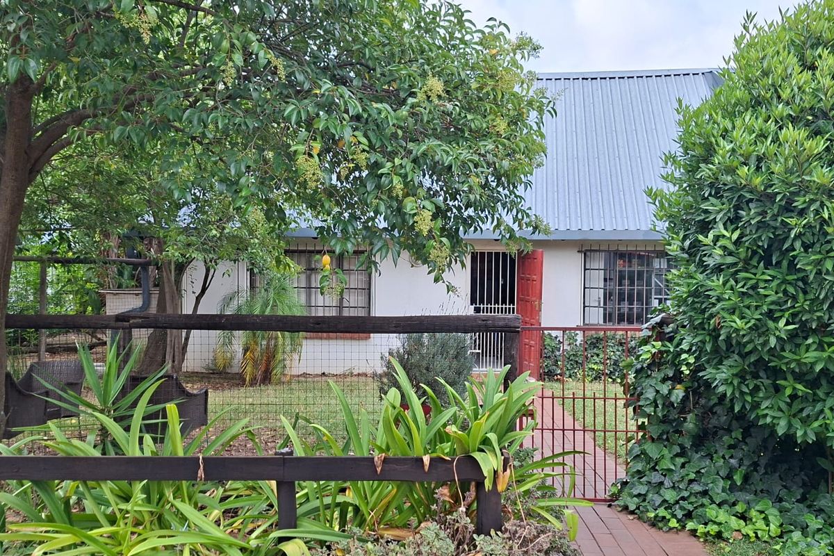 Front view of the property featuring a corrugated metal roof, security gate, and a brick pathway leading to the entrance.