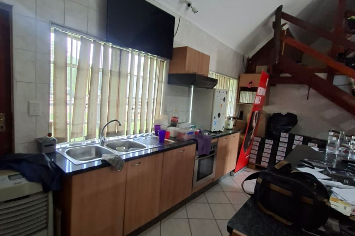 A functional kitchen featuring laminate cabinetry, a double sink, built-in oven, and extractor fan, with tiled flooring and an adjacent staircase.
