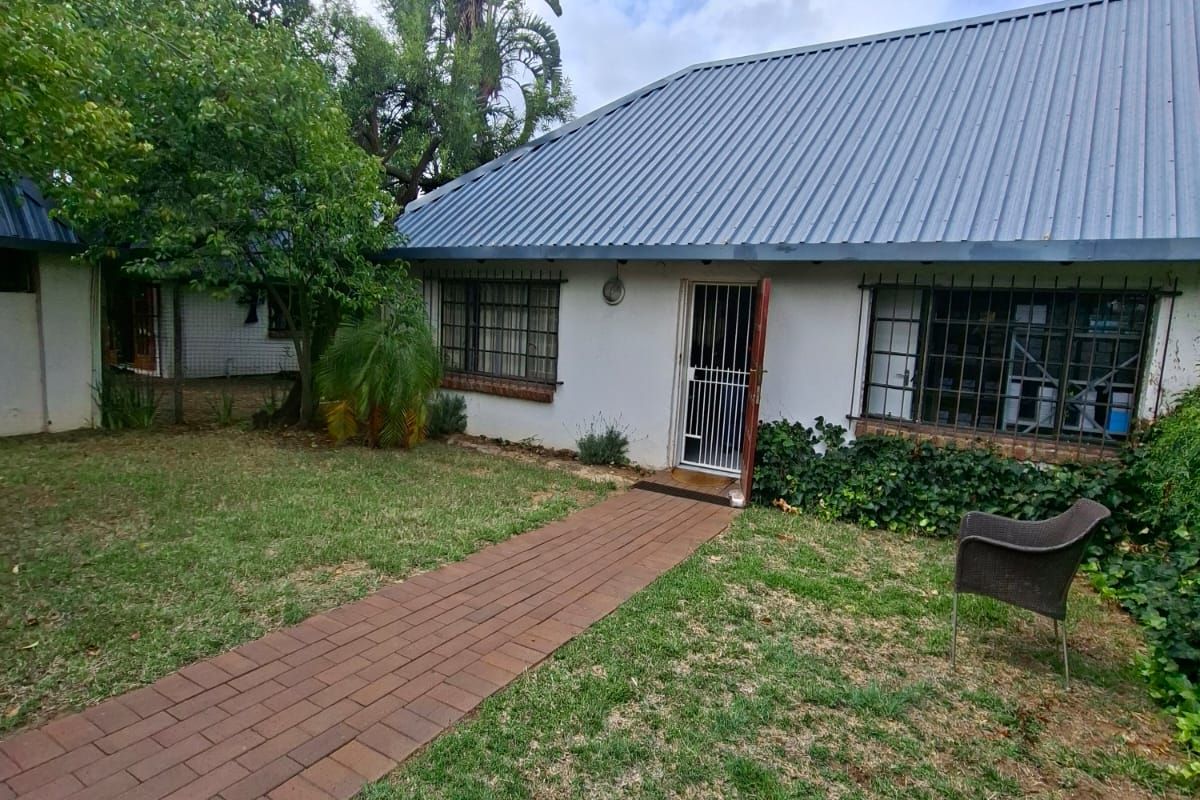 Rear exterior view of the house featuring a metal roof, security bars on windows, and a brick paved walkway leading to the entrance.