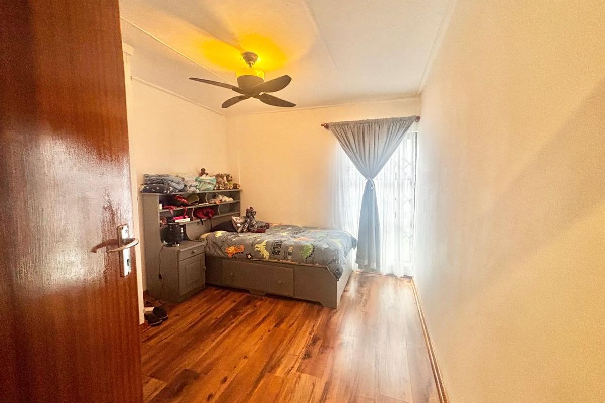 A bedroom featuring laminate flooring, a ceiling fan, and a window with curtains.