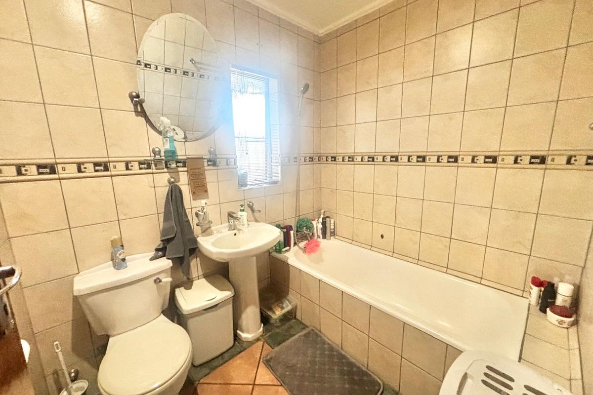 A functional bathroom featuring a pedestal basin, bathtub, and toilet with neutral wall tiling and a decorative border.
