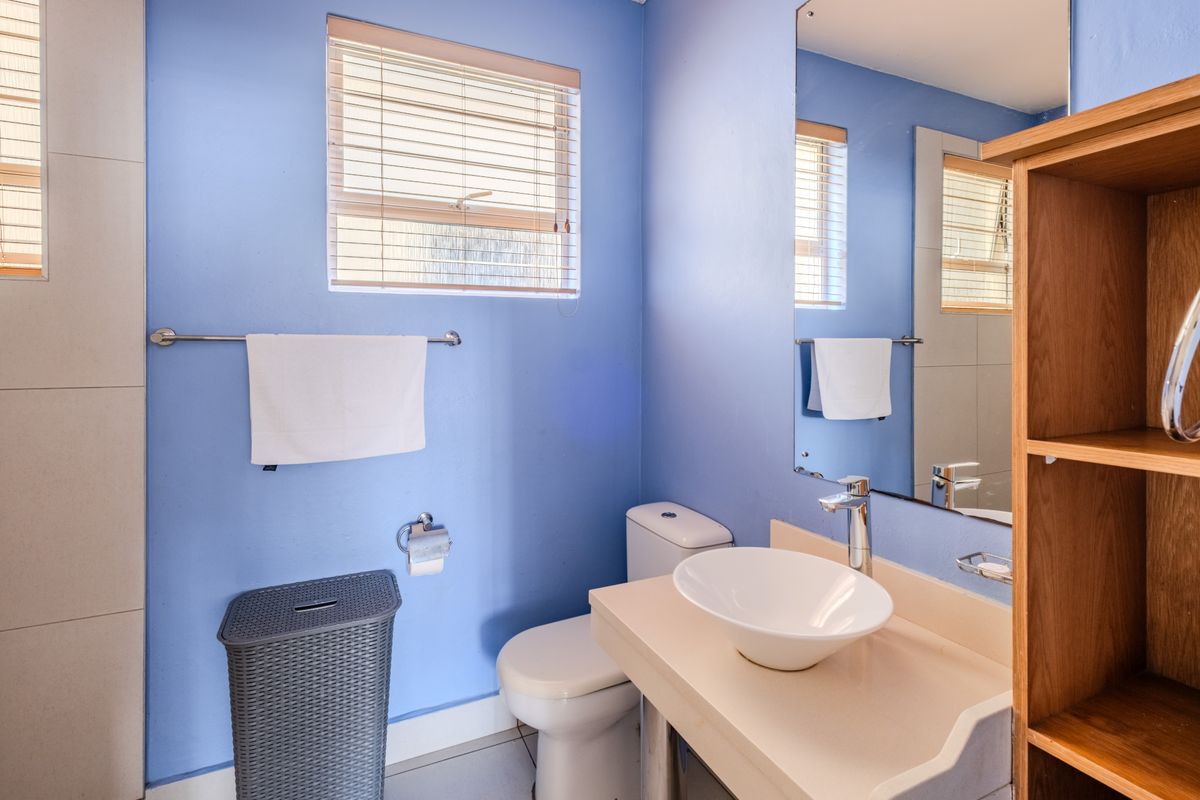 A functional bathroom featuring a vessel sink, chrome faucet, toilet, and wall-mounted mirror with blue painted walls and venetian blinds.