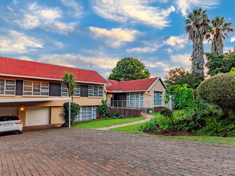 Front elevation of a multi-level residential property featuring a tiled roof, brick driveway, integrated garage, carport, and established garden.