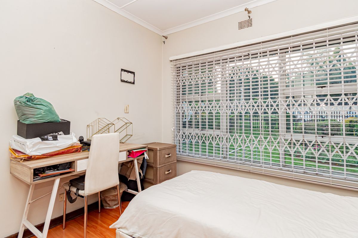 A bedroom featuring laminate flooring and a large window fitted with a security gate, providing natural light and ventilation.