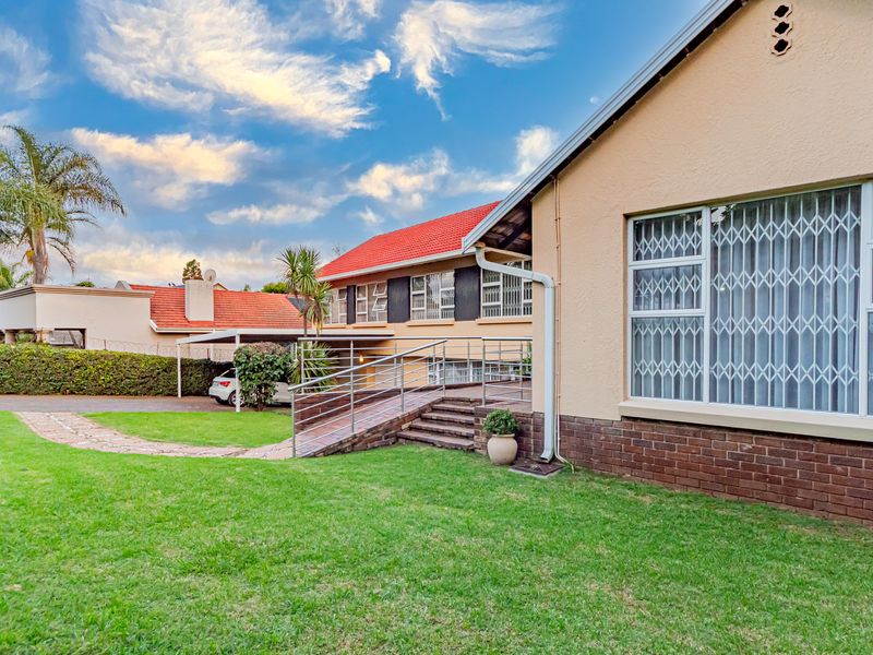 Rear view of the property featuring a well-maintained lawn, brick facade, tiled roof, and a metal accessibility ramp leading to the home.