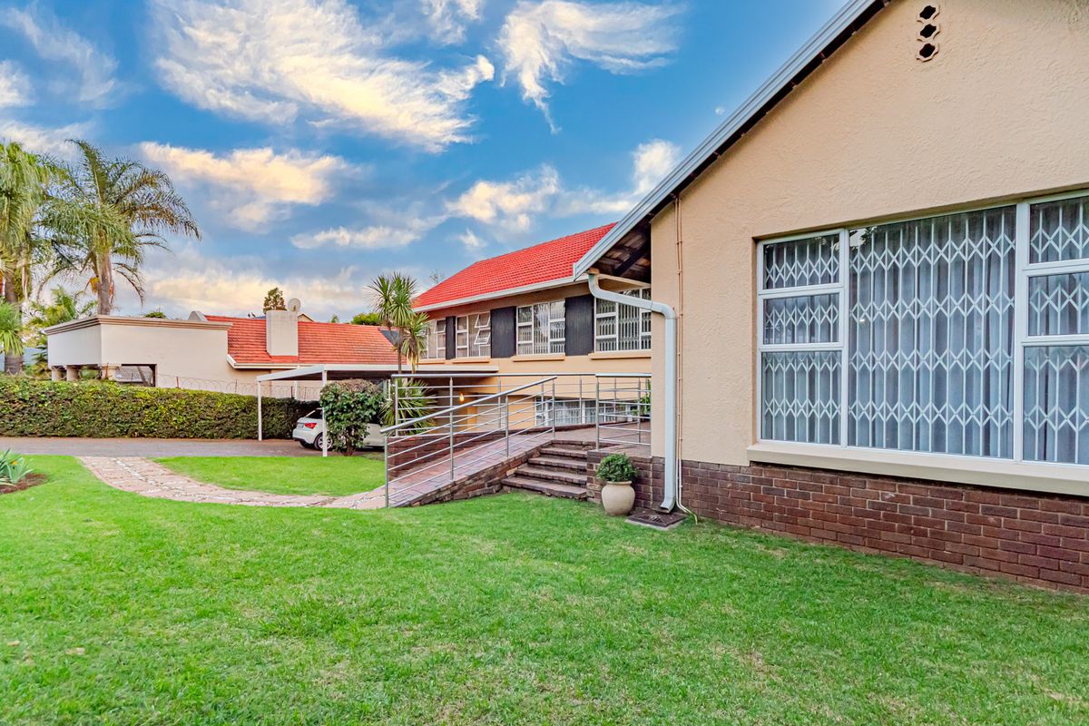 Rear view of the property featuring a well-maintained lawn, brick facade, tiled roof, and a metal accessibility ramp leading to the home.