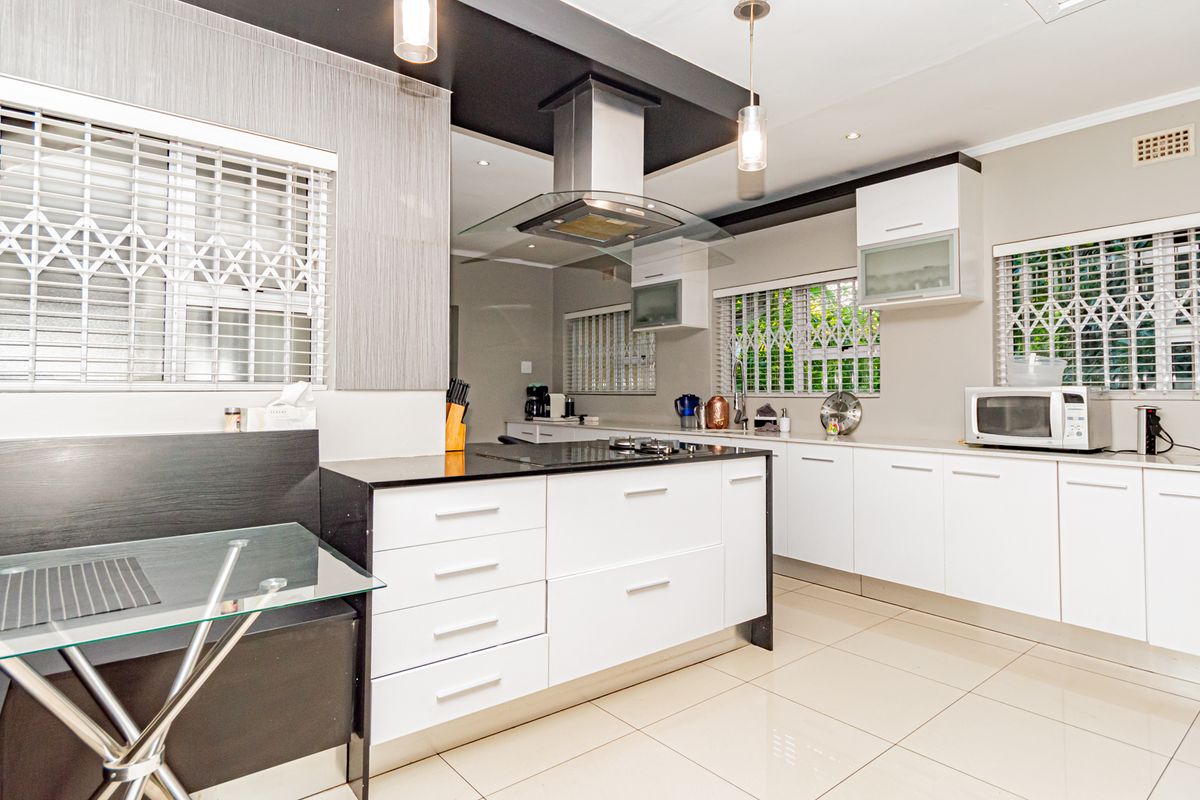 Modern kitchen featuring white cabinetry, a central island with a hob, stainless steel extractor fan, and tiled flooring throughout.