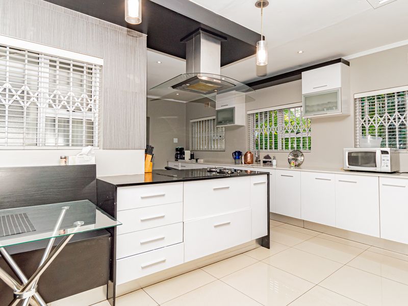 Modern kitchen featuring white cabinetry, a central island with a hob, stainless steel extractor fan, and tiled flooring throughout.