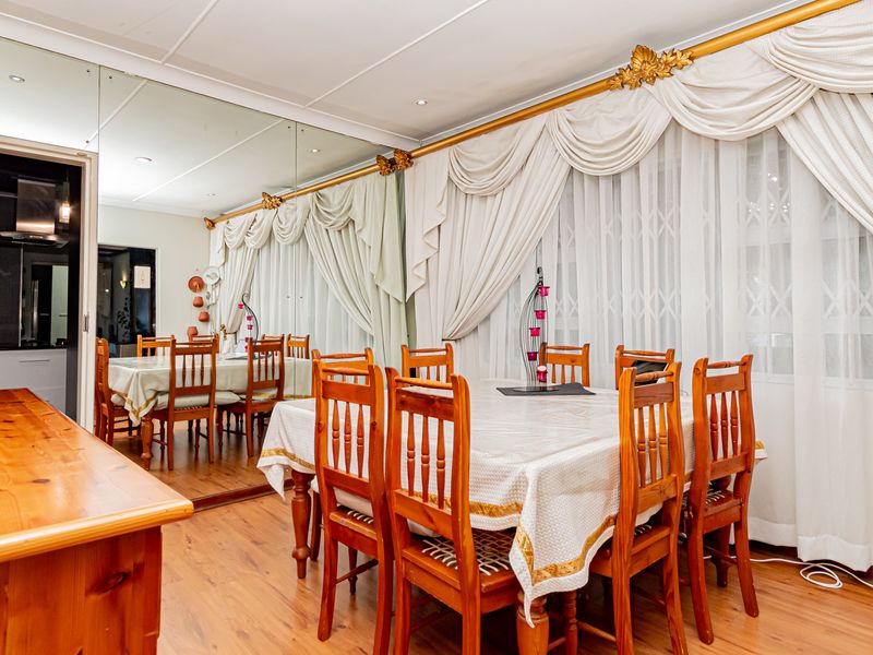 Dining room featuring laminate flooring, a large mirrored wall, and decorative window treatments, with an adjacent view into the kitchen area.