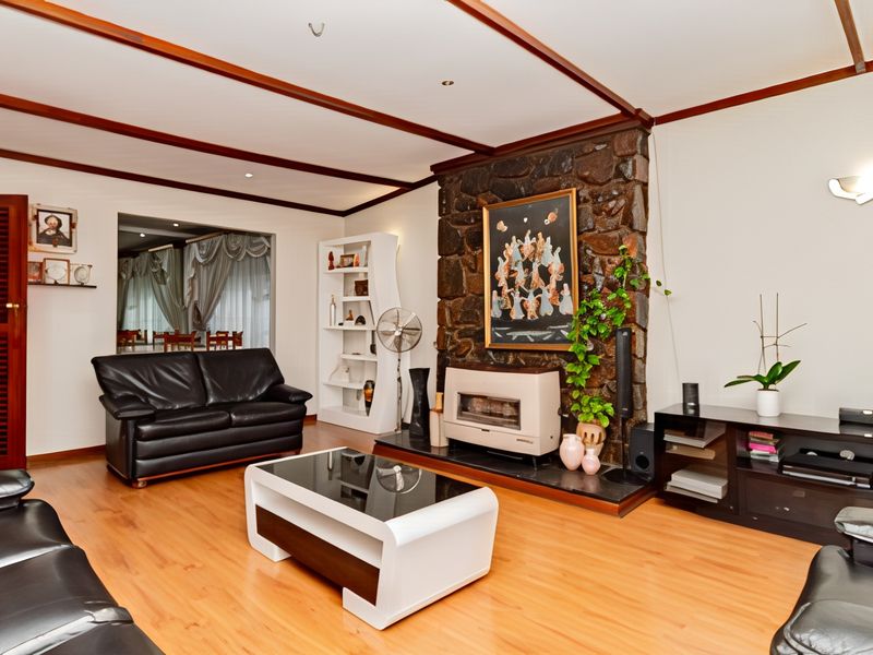 Spacious living room featuring a prominent stone fireplace, timber ceiling beams, and laminate flooring, offering a warm and traditional aesthetic.